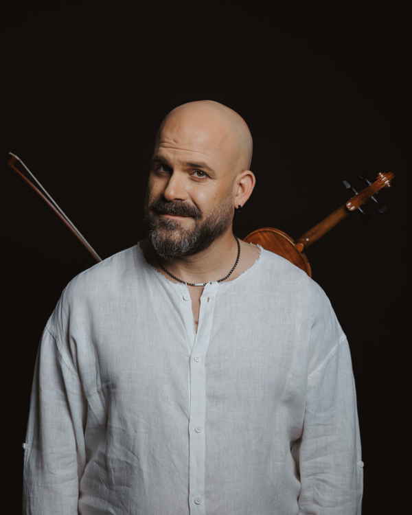 Musician for traditional Greek band for events wearing all white long sleeved shirt and smirking to camera for picture | Altus Entertainment